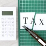 Calculator, scissors, and paper with 'TAX' written on it, symbolizing tax planning and strategies for retirement.